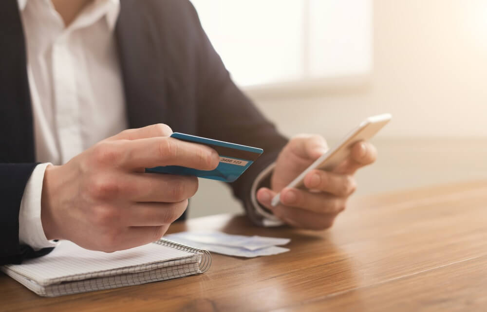- CommuniBee Image of a man holding up his smartphone and credit card.